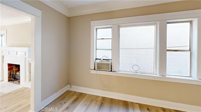 spare room with crown molding, light wood-style floors, a fireplace with flush hearth, cooling unit, and baseboards