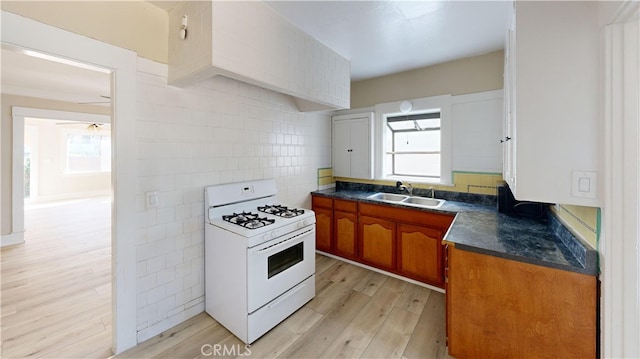 kitchen with dark countertops, a healthy amount of sunlight, white gas range oven, and a sink