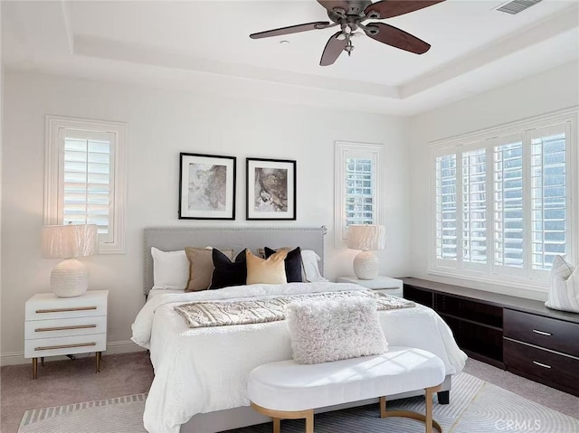 bedroom with a tray ceiling, light colored carpet, visible vents, a ceiling fan, and baseboards