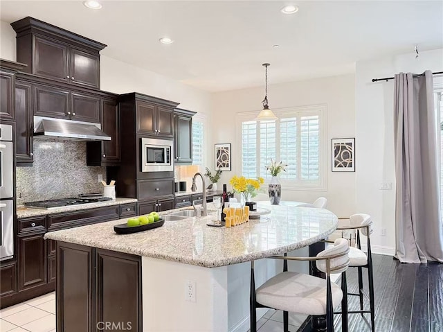 kitchen featuring under cabinet range hood, a sink, a kitchen breakfast bar, appliances with stainless steel finishes, and backsplash