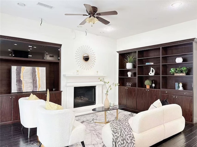 living area with a glass covered fireplace, visible vents, ceiling fan, and wood finished floors