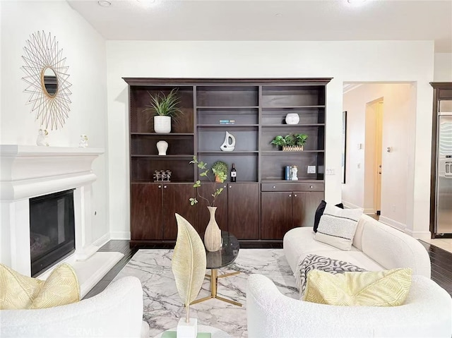 living area featuring a glass covered fireplace, baseboards, and wood finished floors