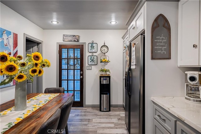 kitchen featuring recessed lighting, black refrigerator with ice dispenser, white cabinets, light stone countertops, and light wood-type flooring