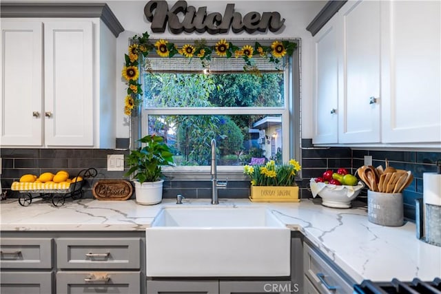 kitchen with tasteful backsplash, a sink, light stone counters, and gray cabinetry