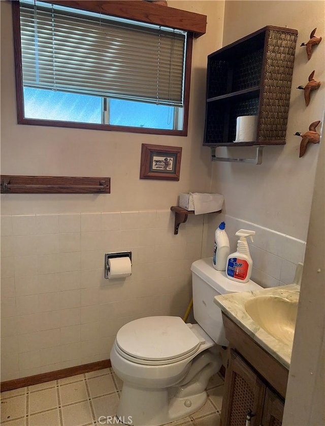 half bath with a wainscoted wall, toilet, tile walls, and vanity