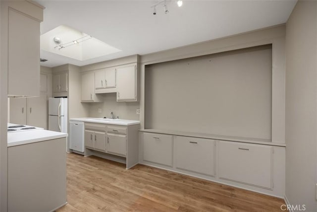 kitchen featuring light wood-style flooring, white appliances, a sink, light countertops, and rail lighting