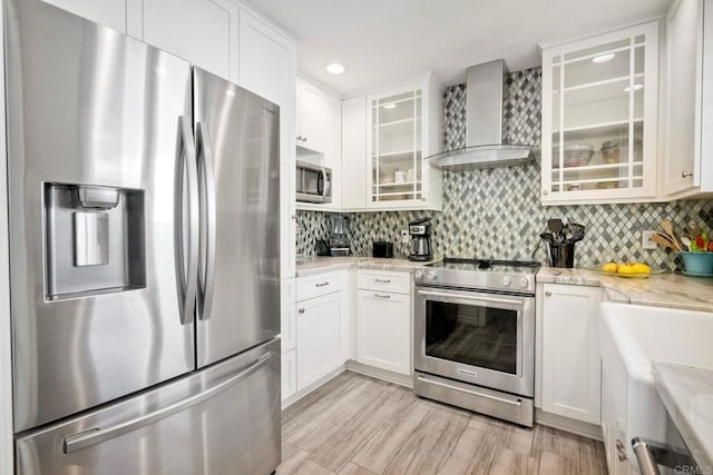 kitchen with decorative backsplash, wall chimney exhaust hood, glass insert cabinets, stainless steel appliances, and white cabinetry