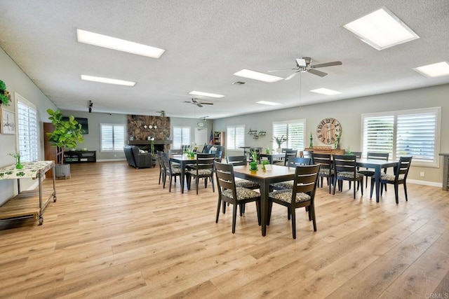 dining area featuring a fireplace, visible vents, a ceiling fan, a textured ceiling, and light wood-type flooring