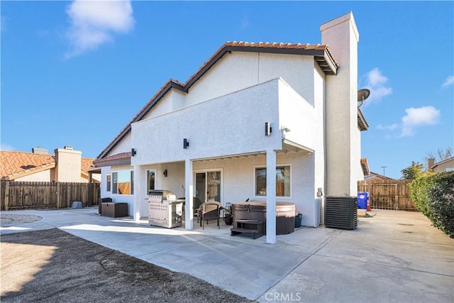 rear view of house featuring stucco siding, a hot tub, a fenced backyard, and a patio