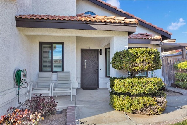 doorway to property with covered porch, a tiled roof, and stucco siding