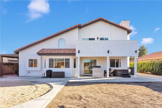 rear view of house featuring fence, a tile roof, stucco siding, a patio area, and a hot tub