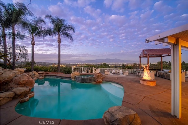 pool at dusk with a fire pit, a patio, fence, and a pool with connected hot tub