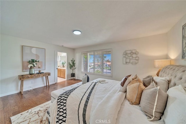 bedroom featuring baseboards, wood finished floors, and ensuite bathroom