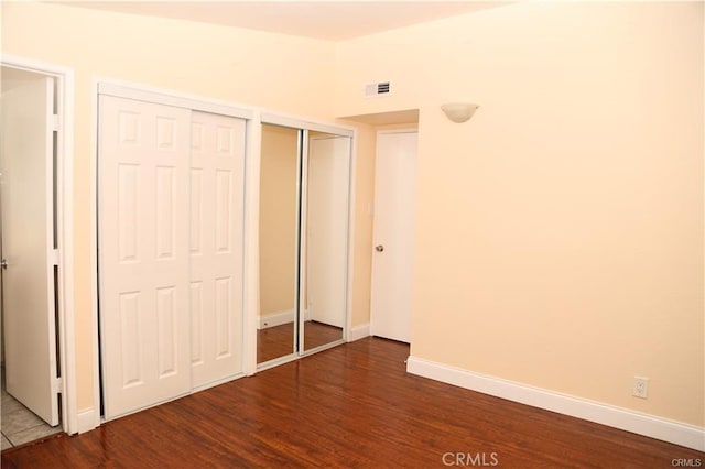 unfurnished bedroom featuring multiple closets, dark wood-style flooring, visible vents, and baseboards