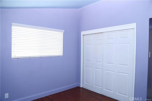 unfurnished bedroom with a closet, dark wood-style flooring, and baseboards