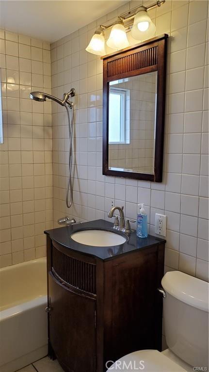 bathroom with decorative backsplash, toilet, shower / tub combination, vanity, and tile walls