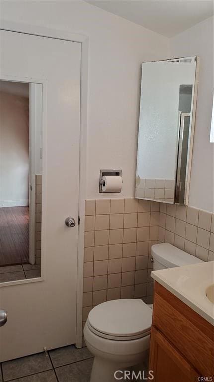 bathroom with tile patterned flooring, toilet, vanity, tile walls, and wainscoting