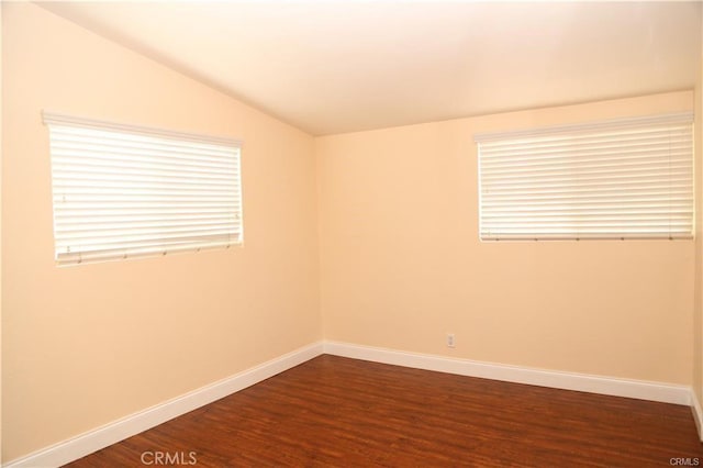 spare room featuring lofted ceiling, baseboards, and dark wood-type flooring