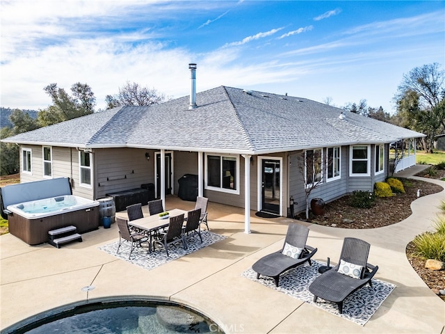 rear view of property featuring outdoor dining space, a hot tub, roof with shingles, and a patio