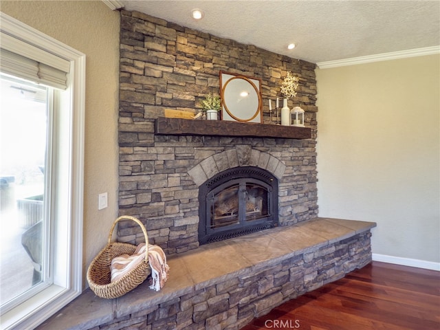 interior details with a textured ceiling, a stone fireplace, wood finished floors, baseboards, and ornamental molding