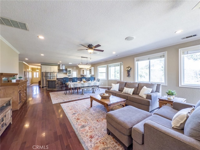 living room with a textured ceiling, visible vents, dark wood finished floors, and crown molding