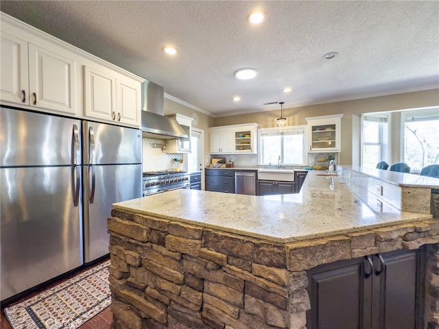 kitchen with stainless steel appliances, backsplash, white cabinets, and wall chimney range hood