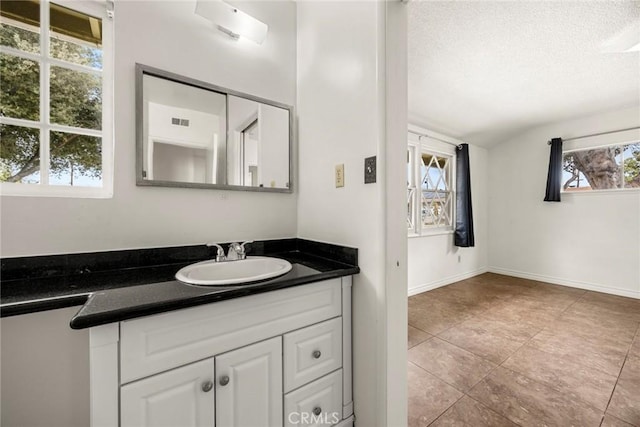 bathroom with baseboards, visible vents, vaulted ceiling, a textured ceiling, and vanity