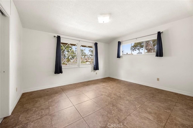 spare room featuring a textured ceiling and baseboards