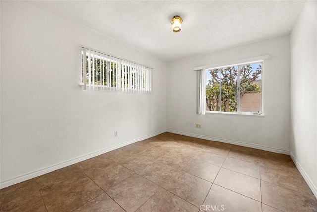 spare room featuring a textured ceiling, a wealth of natural light, and baseboards