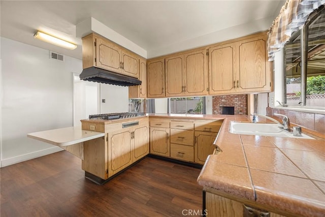 kitchen with tile countertops, a peninsula, dark wood-type flooring, a sink, and visible vents