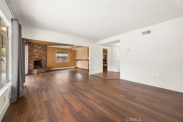 unfurnished living room with dark wood-style floors, baseboards, a brick fireplace, and visible vents