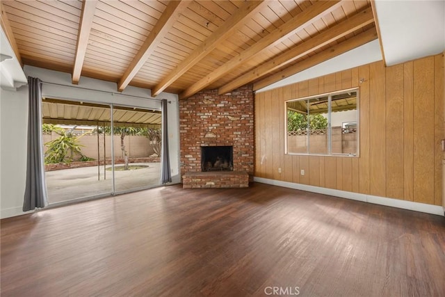 unfurnished living room featuring a fireplace, lofted ceiling with beams, wooden walls, wood finished floors, and baseboards