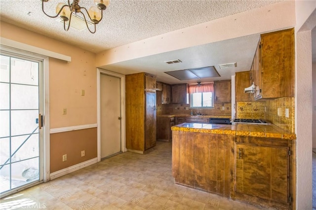 kitchen featuring a peninsula, tasteful backsplash, visible vents, and brown cabinetry