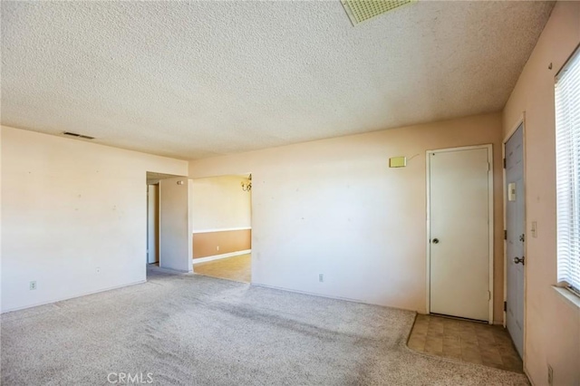 spare room with carpet, visible vents, and a textured ceiling