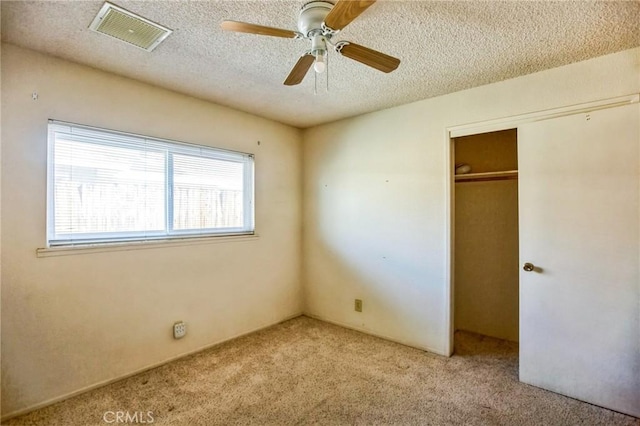 unfurnished bedroom featuring a textured ceiling, carpet flooring, visible vents, a ceiling fan, and a closet