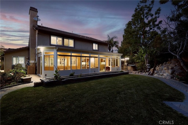 back of property at dusk with a sunroom, a yard, and stucco siding