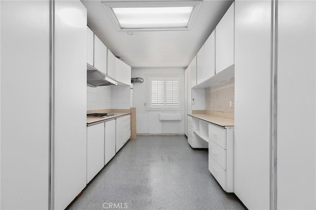 kitchen with stainless steel gas cooktop, freestanding refrigerator, light countertops, under cabinet range hood, and white cabinetry