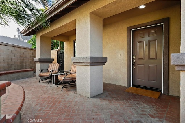 view of exterior entry featuring a patio, fence, and stucco siding