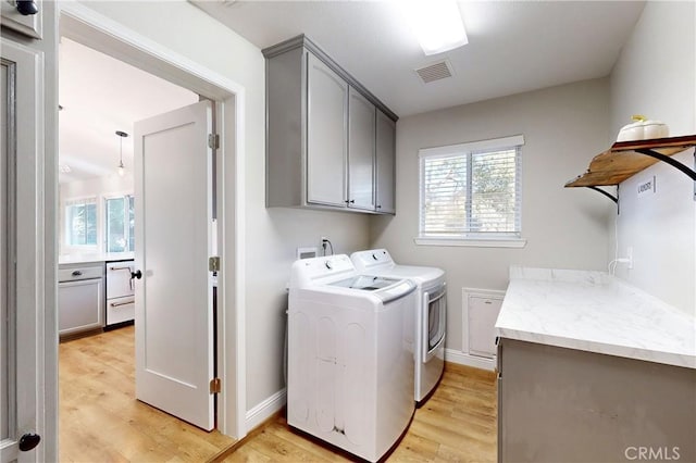 washroom with light wood-style flooring, visible vents, baseboards, independent washer and dryer, and cabinet space