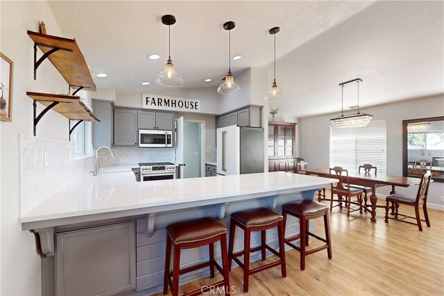 kitchen with a peninsula, high end appliances, a sink, and gray cabinetry