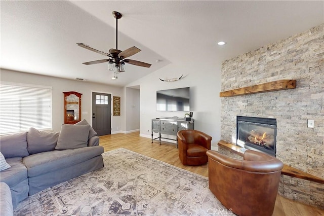 living area with a ceiling fan, lofted ceiling, a stone fireplace, and wood finished floors