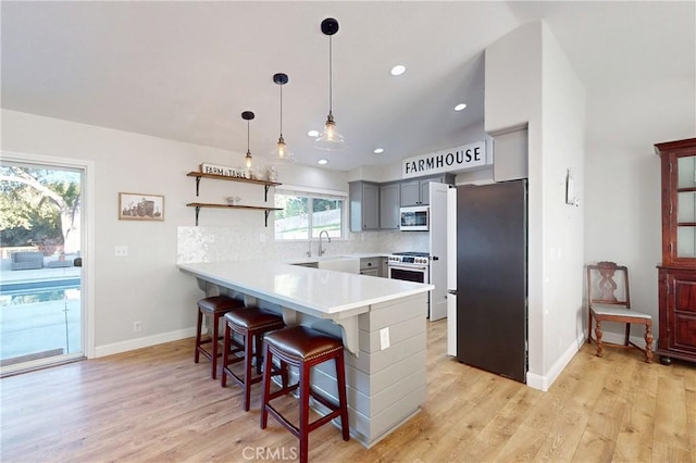 kitchen with light wood finished floors, stainless steel appliances, decorative backsplash, a peninsula, and a kitchen bar