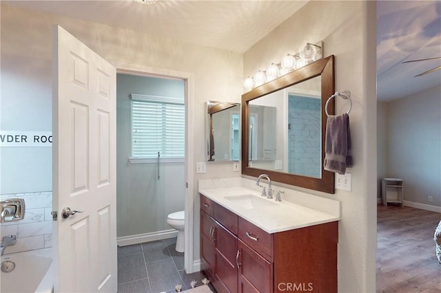 bathroom with toilet, a bathing tub, vanity, wood finished floors, and baseboards