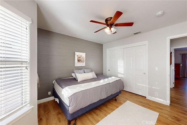 bedroom featuring visible vents, an accent wall, light wood-type flooring, multiple windows, and baseboards