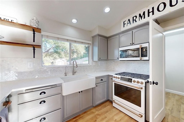 kitchen with gray cabinets, light wood-style flooring, decorative backsplash, a sink, and white appliances