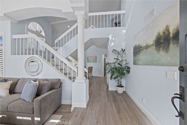 foyer entrance featuring visible vents, baseboards, stairway, a towering ceiling, and wood finished floors