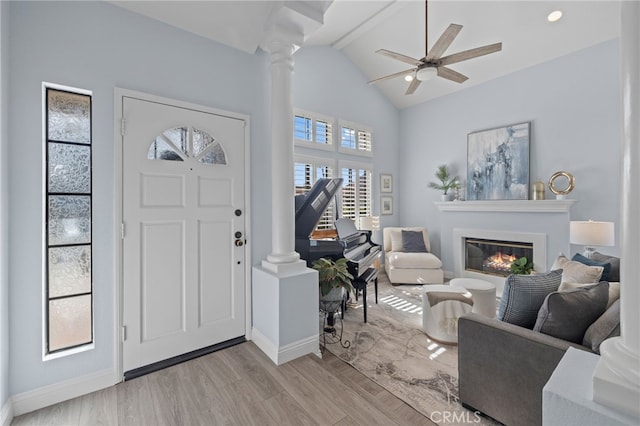 entrance foyer with light wood finished floors, a glass covered fireplace, lofted ceiling, and decorative columns