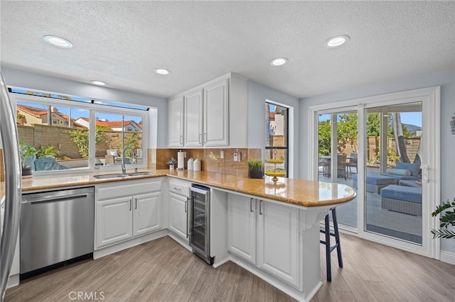 kitchen with beverage cooler, dishwasher, a peninsula, white cabinetry, and a sink