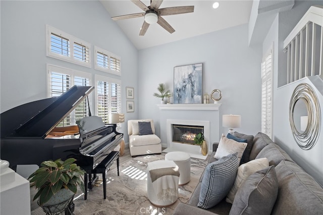 sitting room with ceiling fan, high vaulted ceiling, and a glass covered fireplace