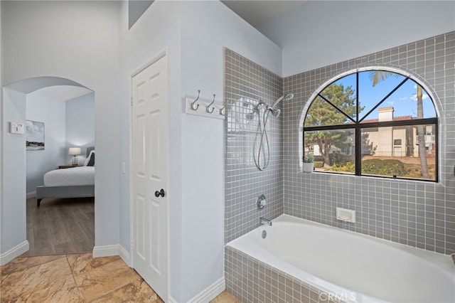 ensuite bathroom featuring baseboards, marble finish floor, ensuite bath, and tiled shower / bath combo